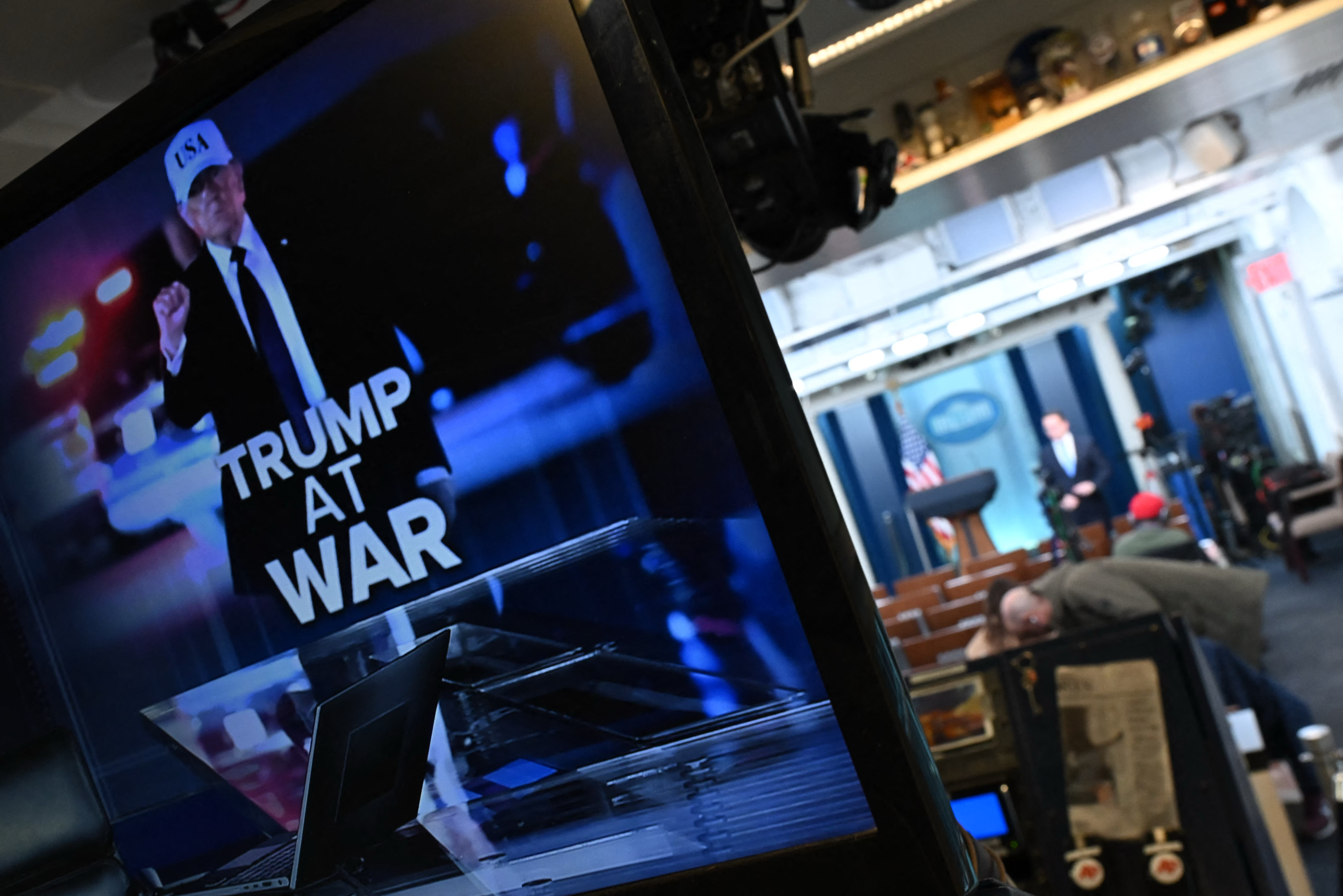 Reporters are seen in the briefing room near a TV monitor