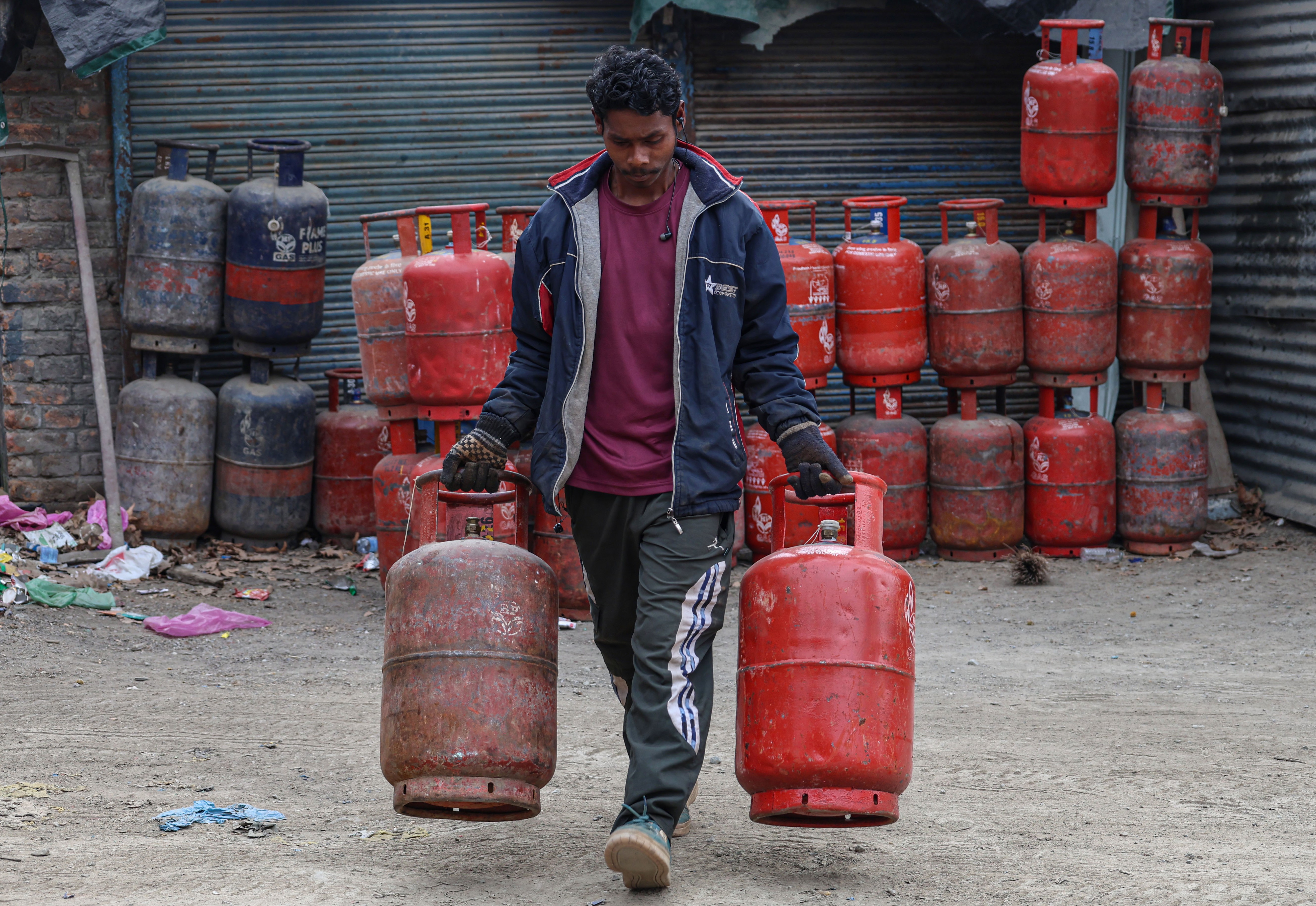 A man carries two gas canisters from a pile behind him.