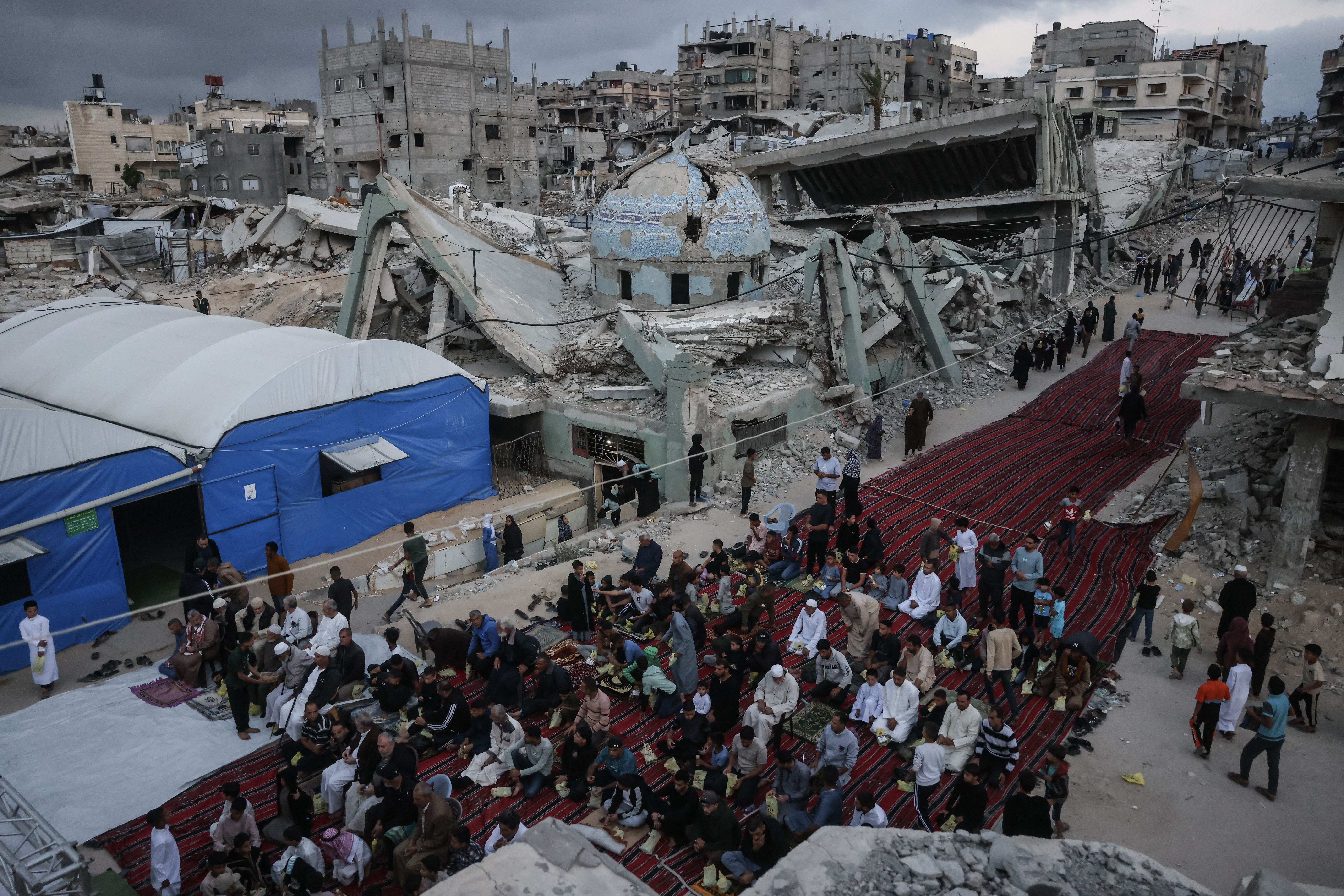 TOPSHOT - Palestinians gather on a heavily damaged street to perform morning prayers marking the start of Eid al-Adha, the Feast of Sacrifice, in Khan Yunis in the southern Gaza Strip on May 27, 2026.
