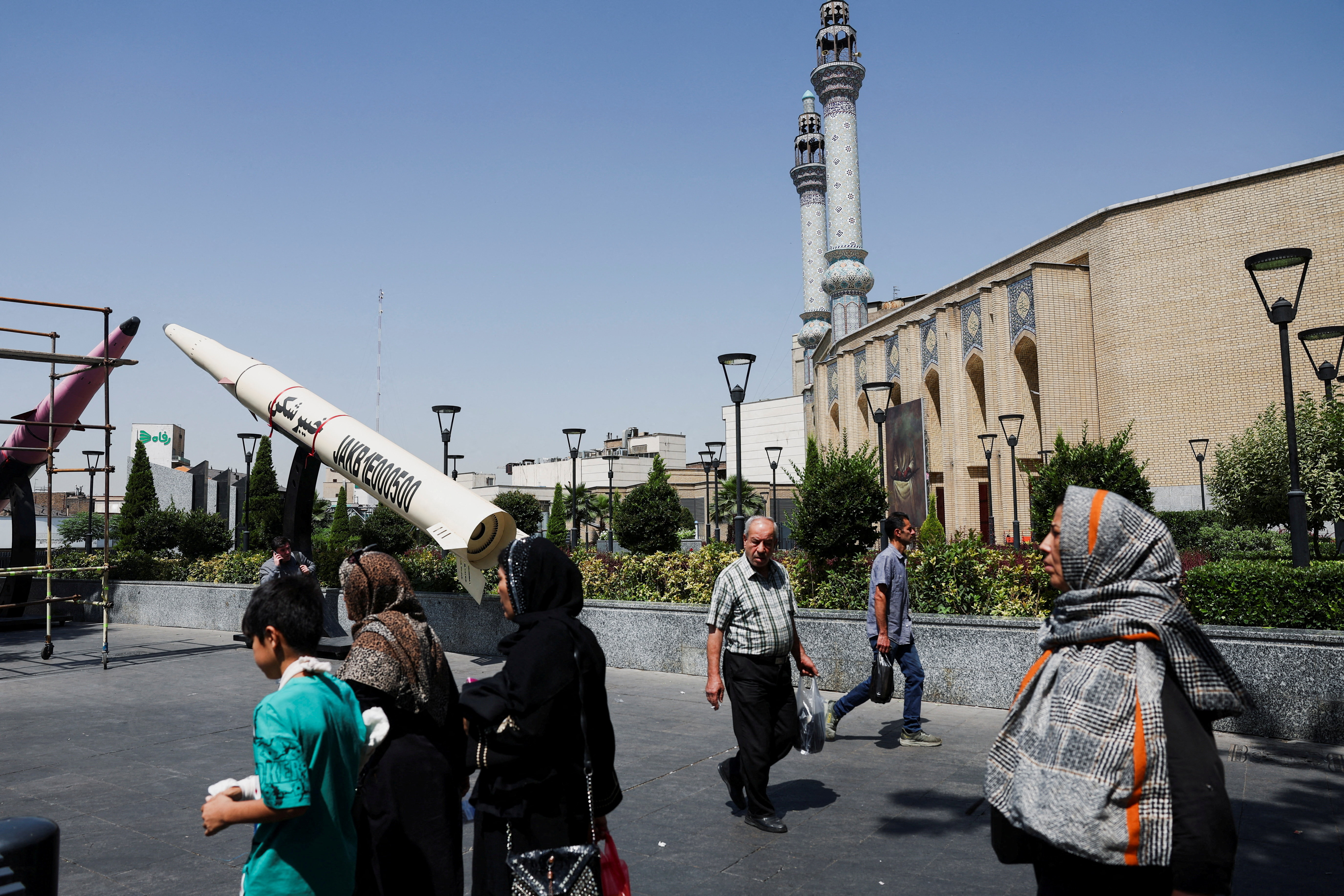 People walk on a street next to a symbolic mock-up of an Iranian missile.