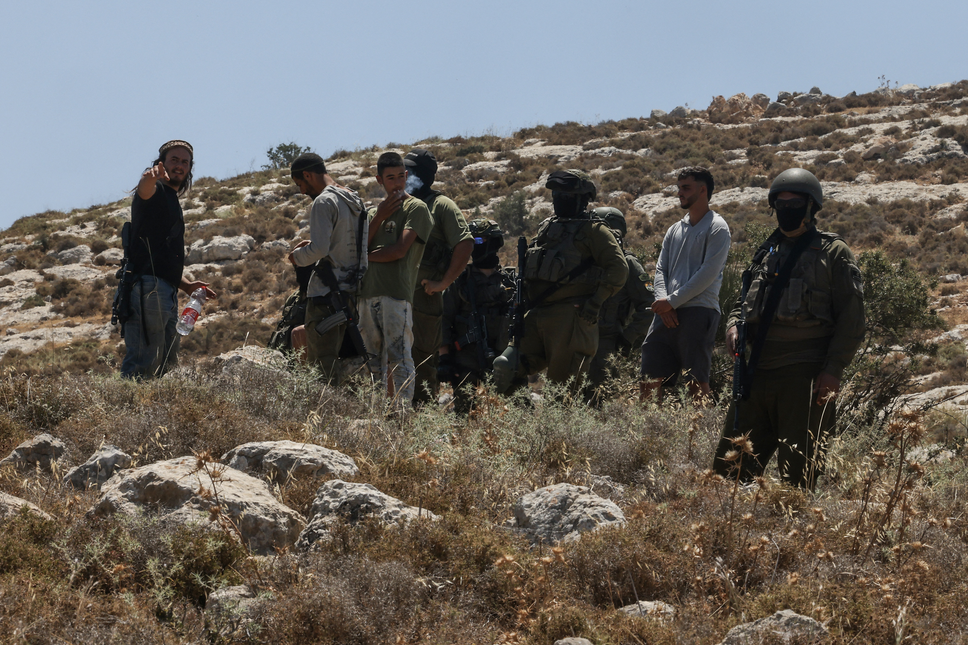 Israeli forces and armed settlers guard a bulldozer reportedly operating on Palestinian lands as local Palestinian landowners (unseen) gather in protest against land confiscations near the village of Dura, west of Hebron in the Israeli-occupied West Bank, on June 9, 2026.