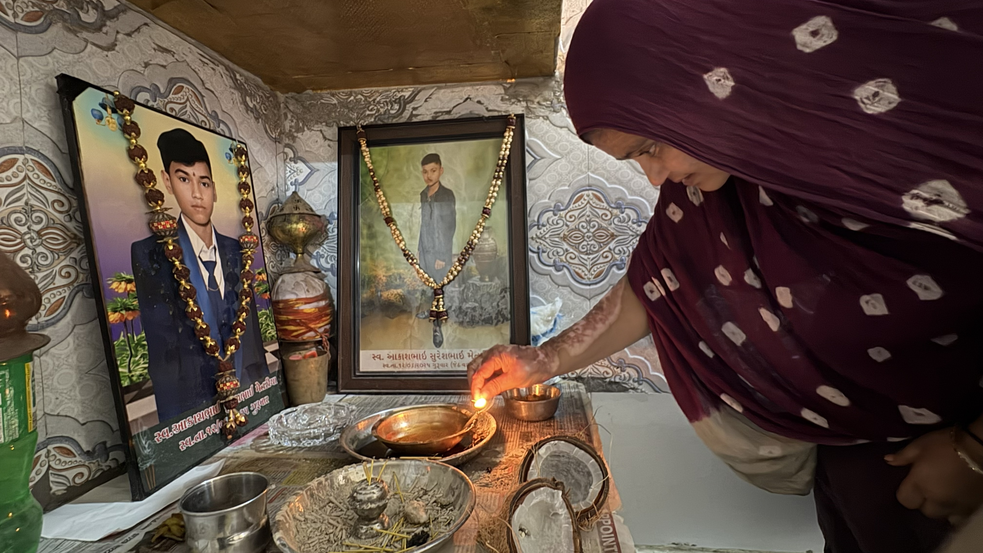 Sita Patni lights an oil lamp in front of photos of her son Aakash, killed when the plane crashed near her tea stall in Ahmedabad, India [Marhaba Hilali/ Al Jazeera]