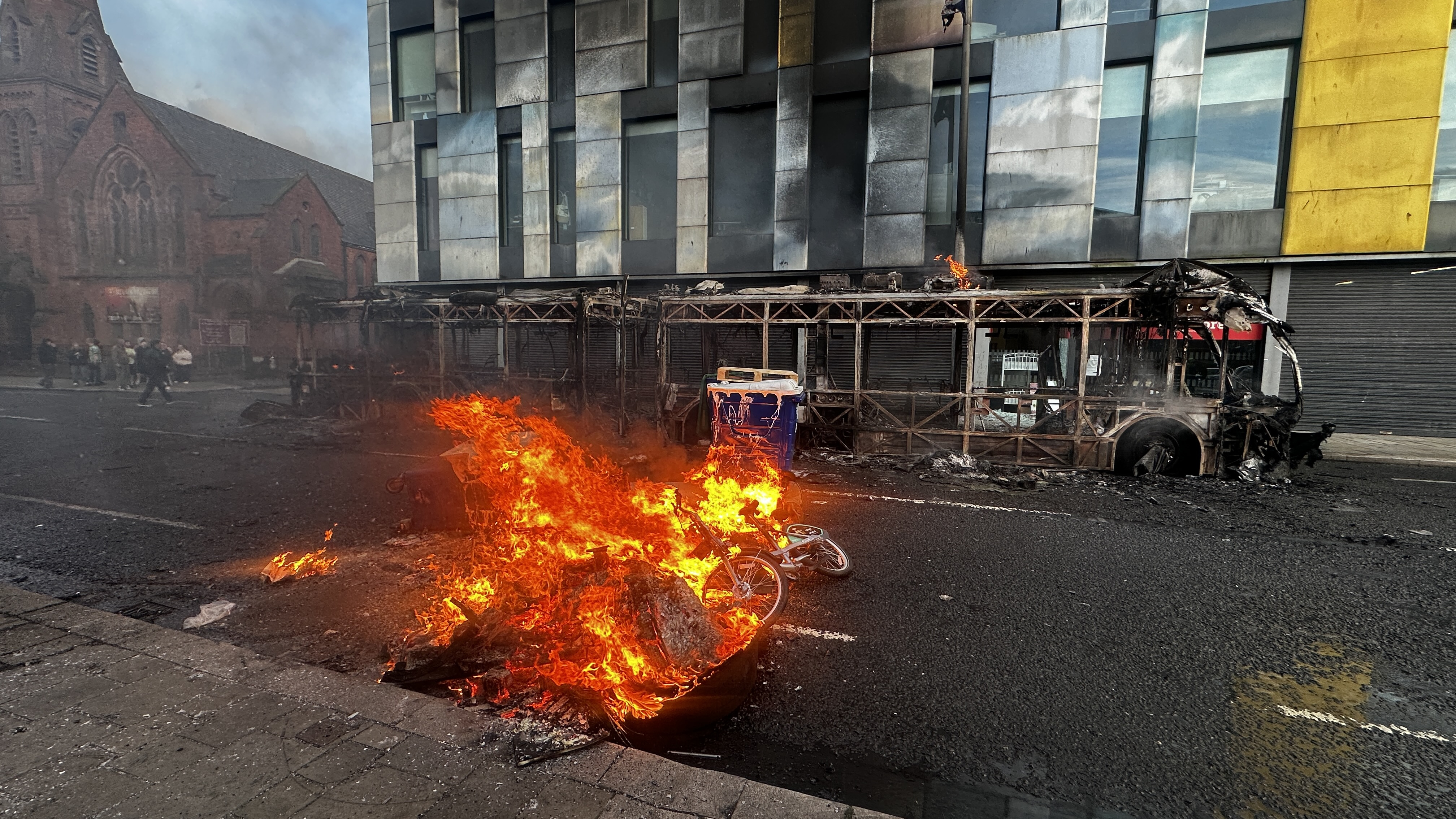 The skeleton of a Glider bus, set fire by protesters, on the Newtownards Road in east Belfast, as disorder flared during an anti-immigration demonstration organised in response to Monday night's stabbing attack in the city. A 30 year-old man arrested in connection with the Belfast stabbing attack has been charged with attempted murder and will appear in court in the city on Wednesday, the Police Service of Northern Ireland has said. Picture date: Tuesday June 9, 2026. [PA Images via Getty Images]