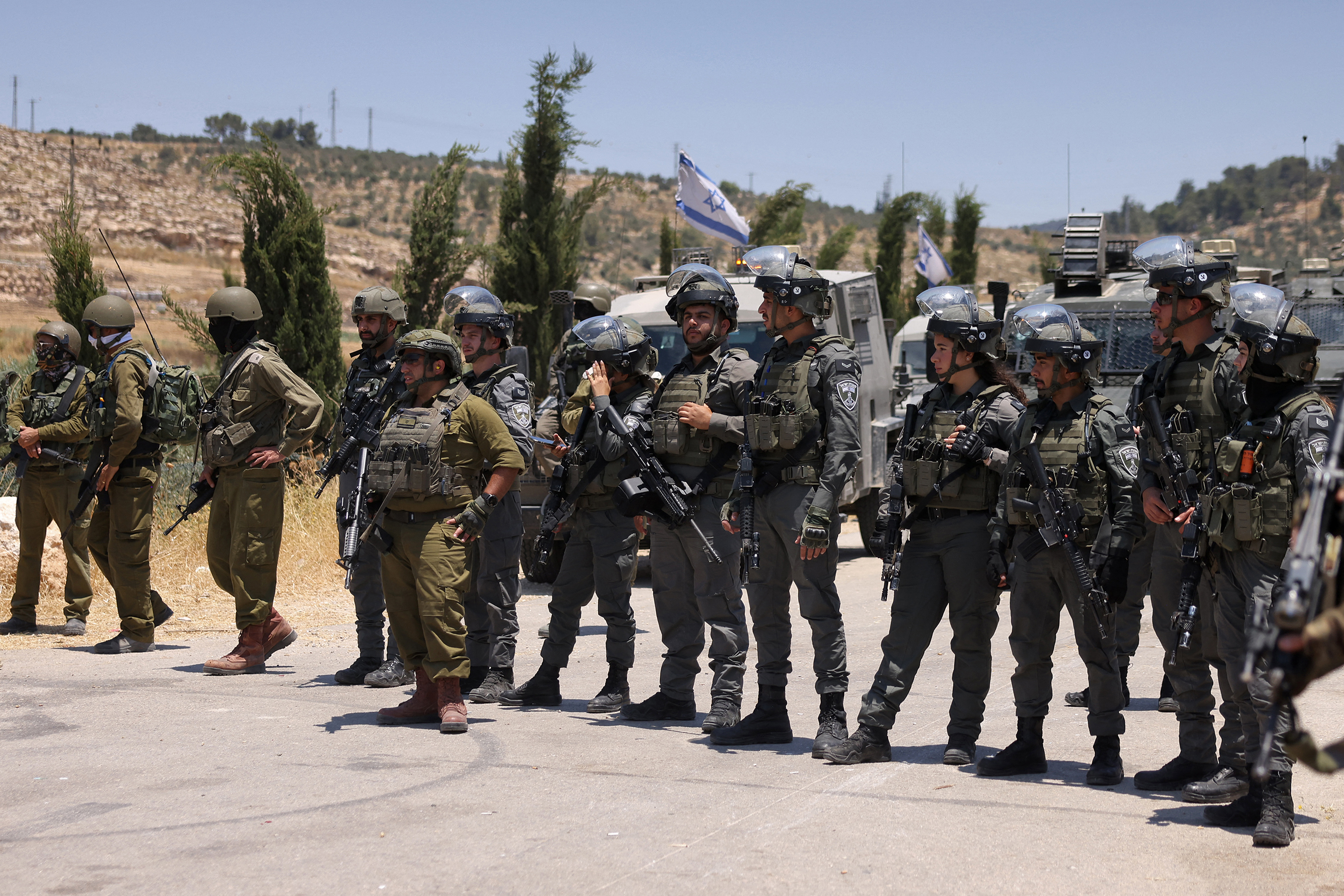 Israeli security forces stand guard as Palestinians gather to protest threats of confiscation of their land in the Palestinian village of Idna, west of Hebron in the occupied West Bank, on June 12, 2026.
