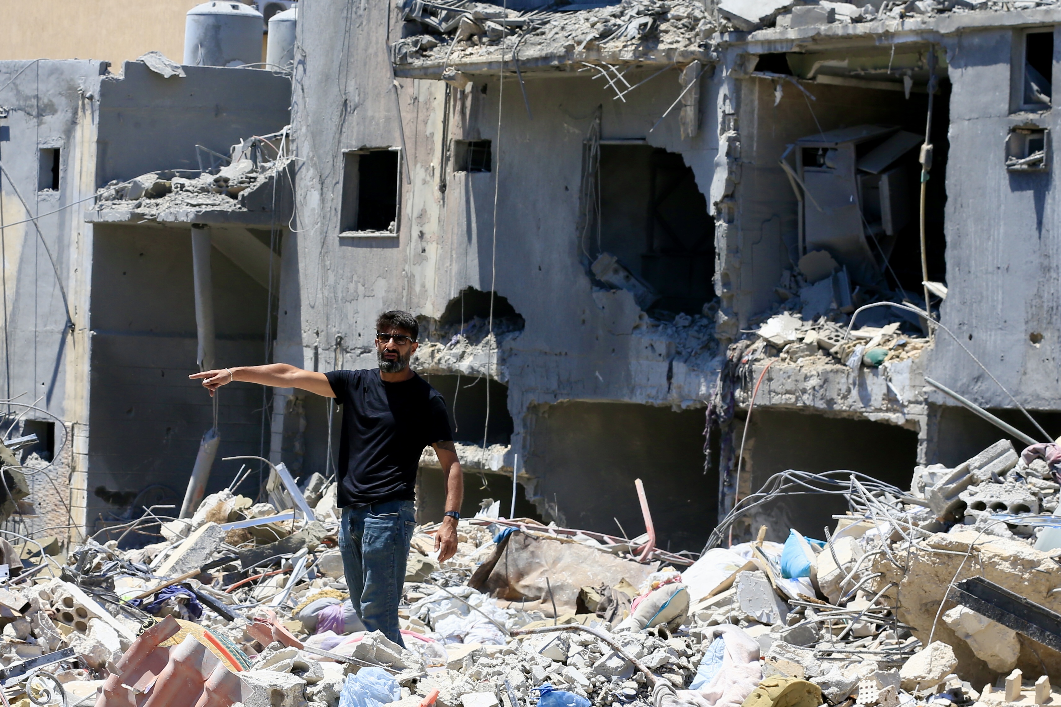 A man inspects a damaged building with piles of rubble.