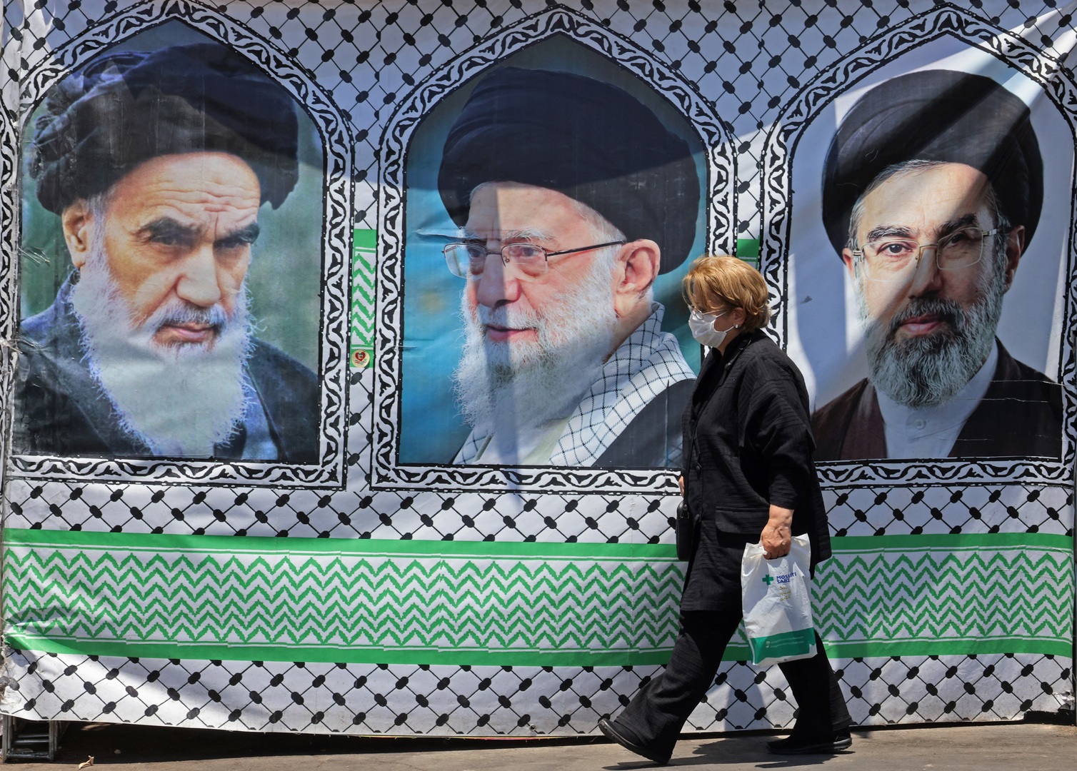 A woman walks past a banner bearing the images of the late founder of the Islamic Revolution supreme leader Ayatollah Ruhollah Khomeini (L), the late Iranian supreme leader Ali Khamenei and his son, the current supreme leader Mojtaba Khamenei (R), erected along a street at the Vanak Square in Tehran on June 10, 2026. [Atta Kenare/AFP]