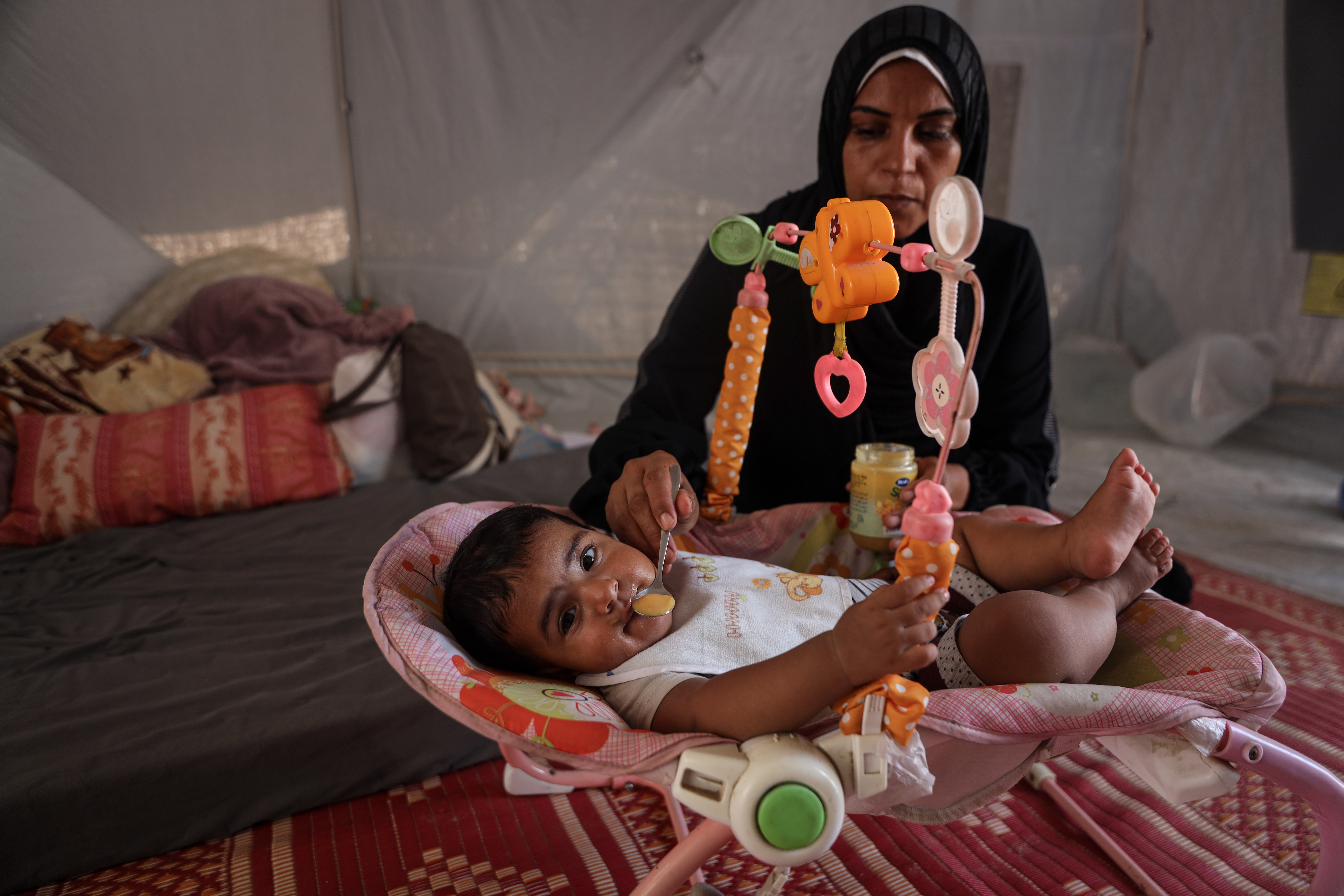 Eman Huneidq, 38, breastfeeds her nine-month-old daughter, Ward, while living in displacement in Deir al-Balah [Abdelhakim Abu Riash/ Al Jazeera]