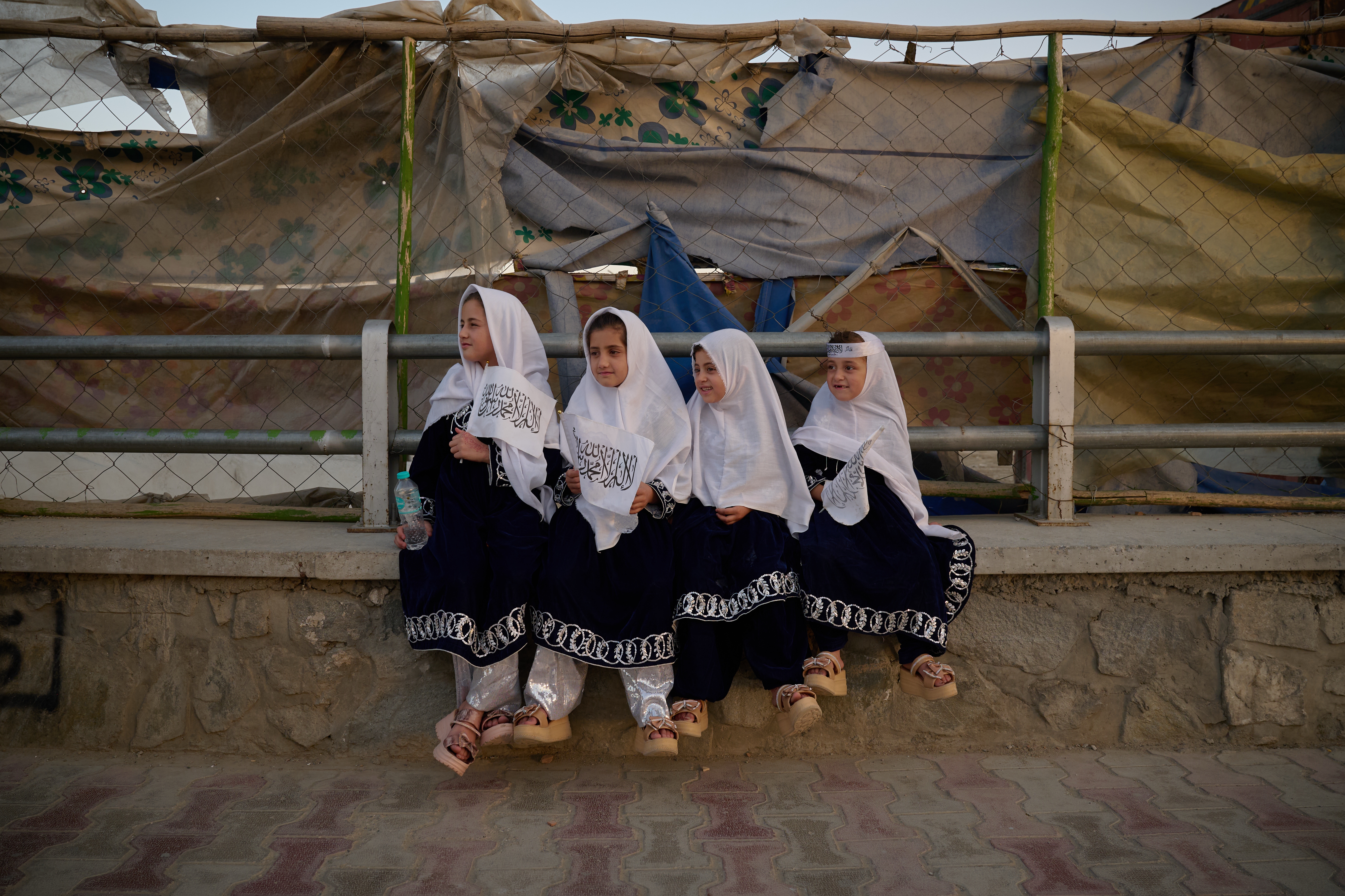 Four young girls dressed in matching outfits hold Taliban flags on the eve of the fifth anniversary of the U.S. withdrawal