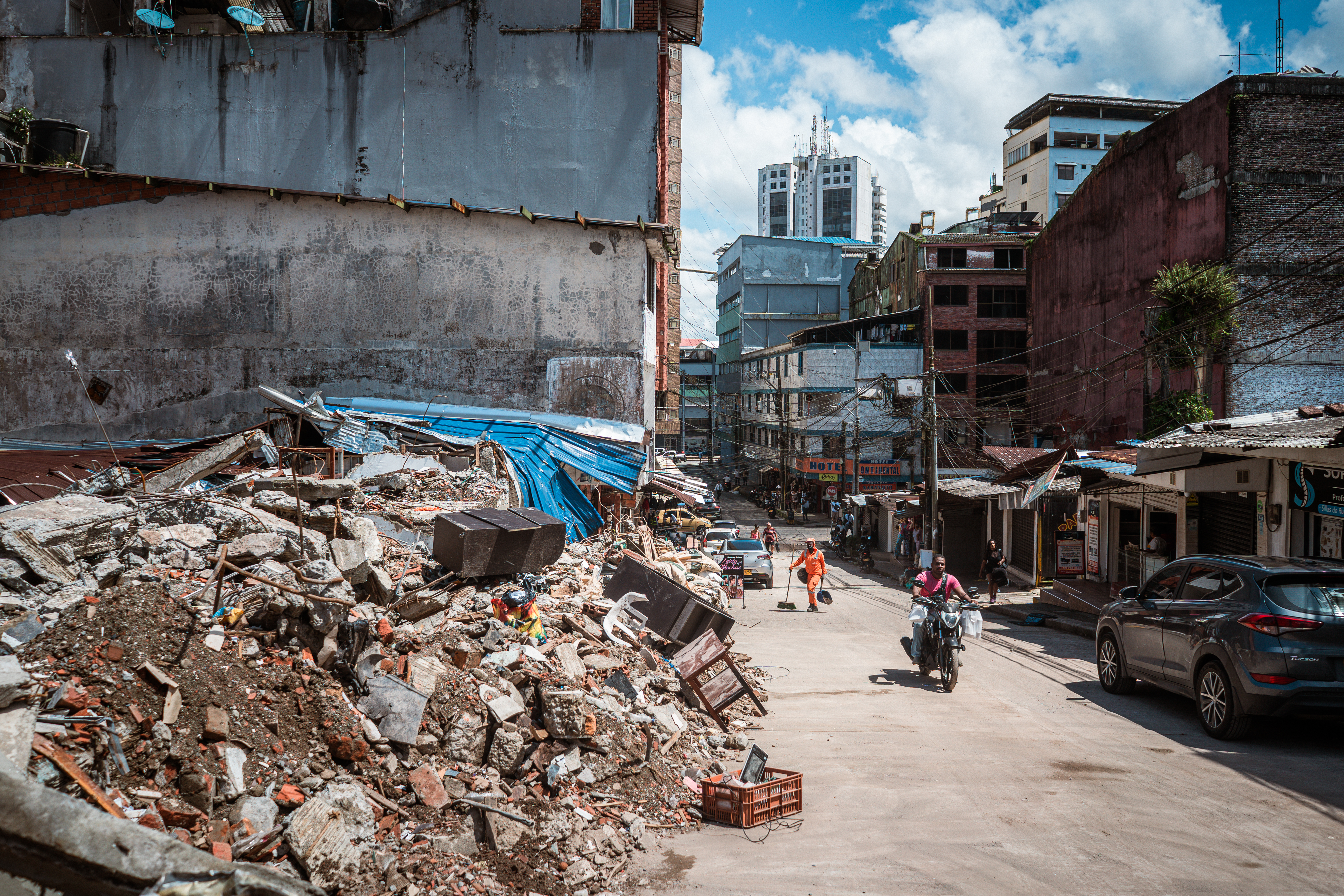 Motorists and pedestrians pass by the wreckage of a collapsed building on a street in Buenaventura. [Euan Wallace / Al Jazeera]