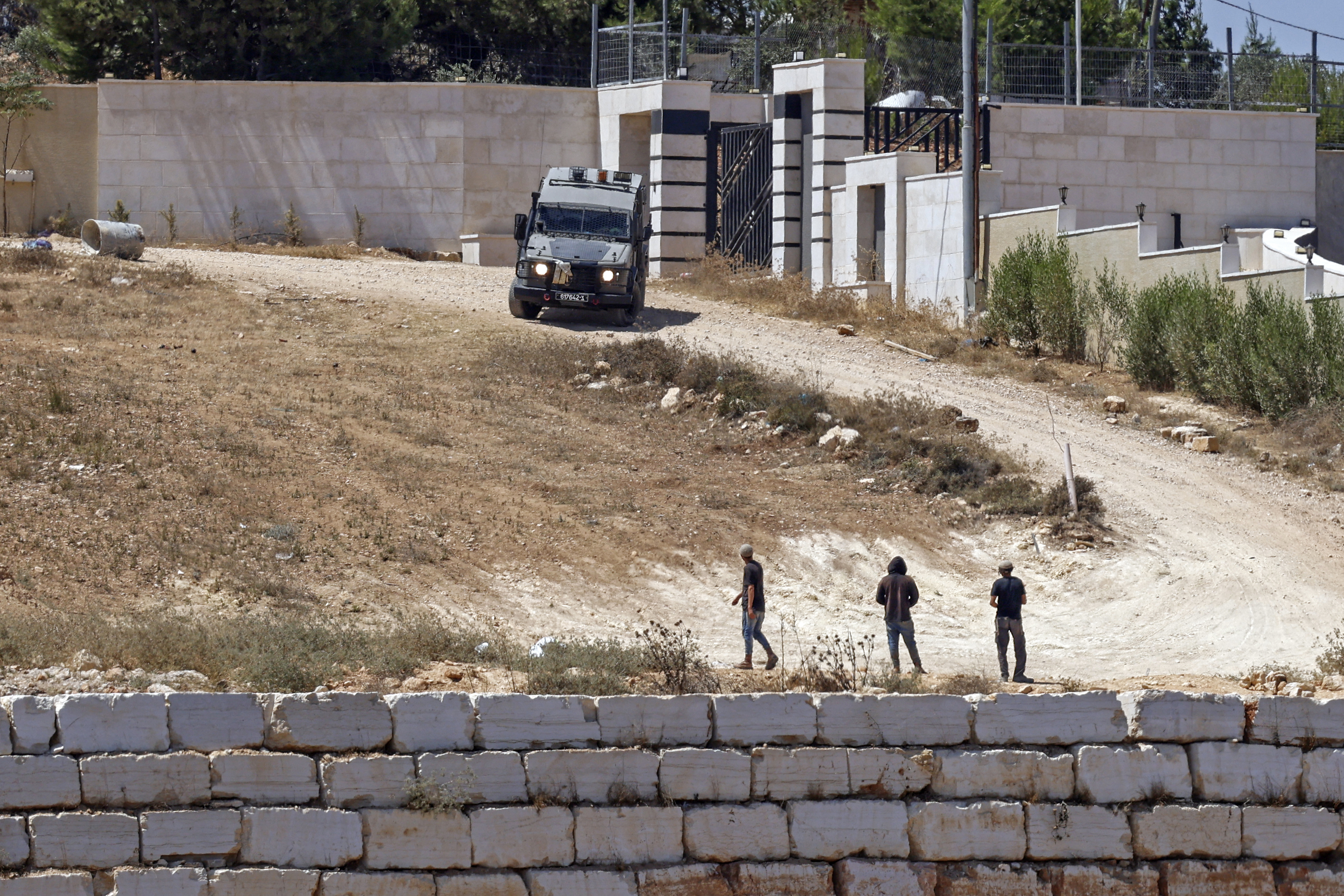 An Israeli military vehicle patrols near to the settlers in front of the Palestinian houses in the village of Qusra, south of Nablus, in the occupied West Bank, on August 13, 2026.