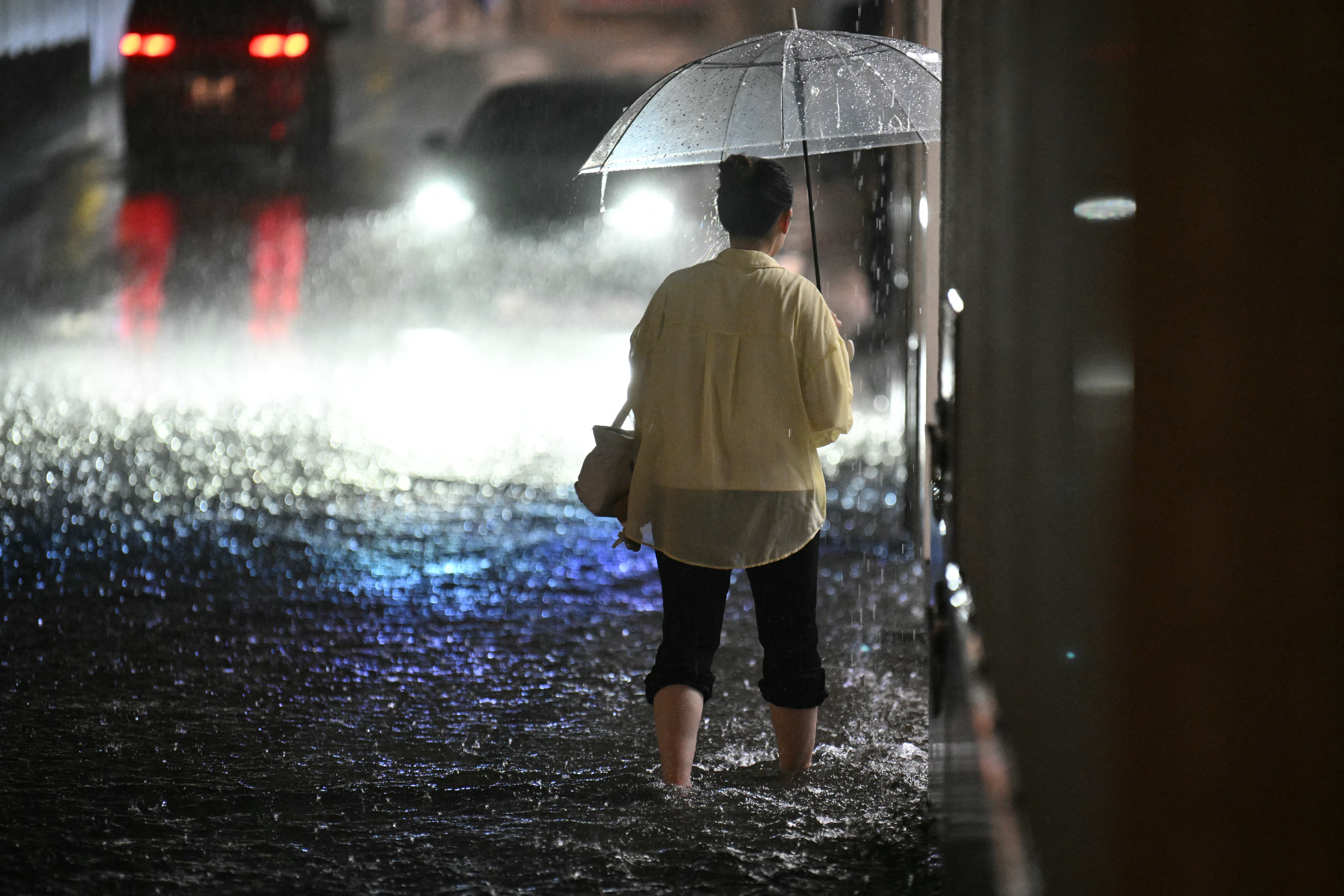 A woman wades through a flooded road near Chiba metro station in Chiba on August 13, 2026, as heavy rain swept through the area.