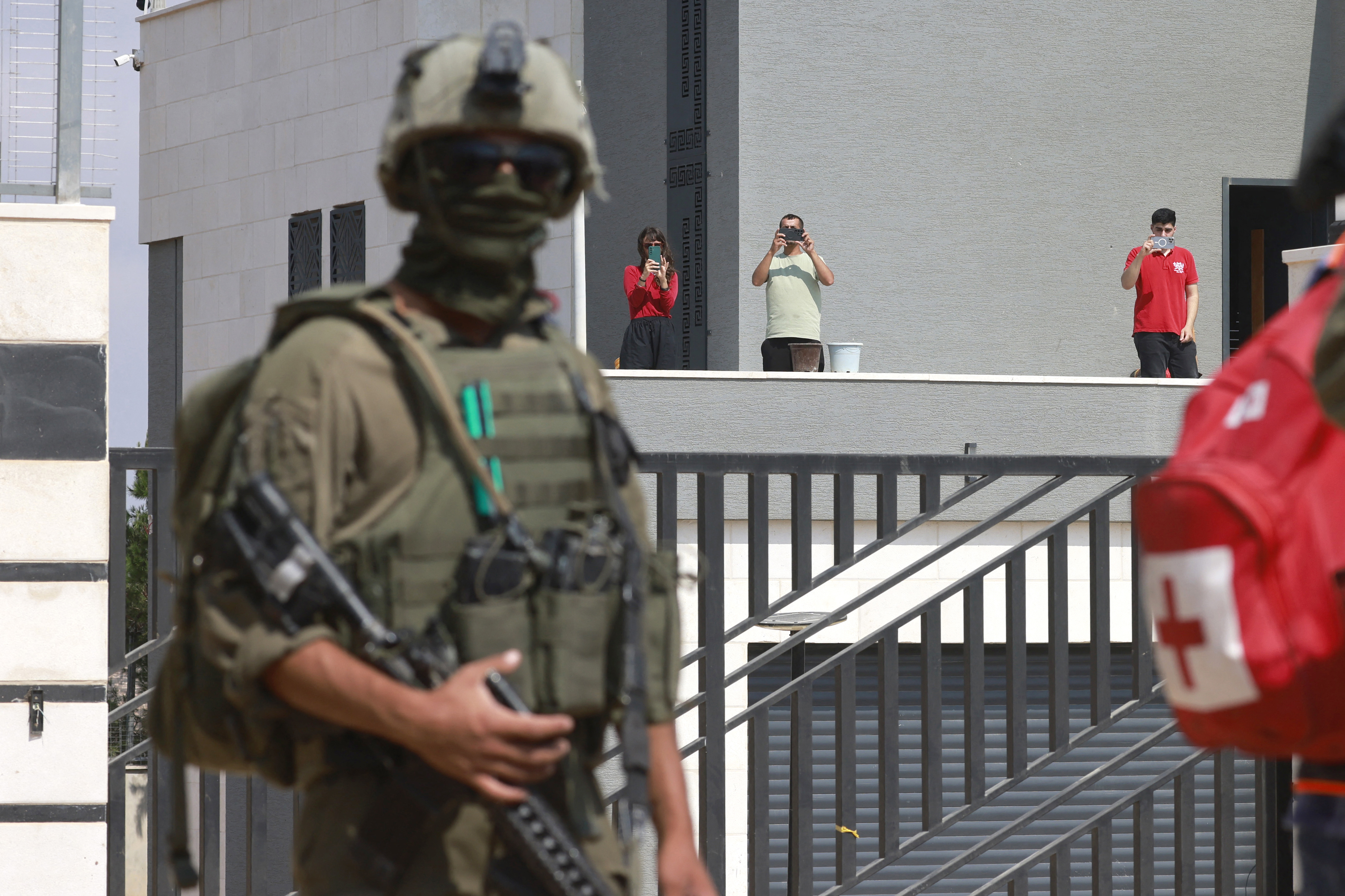 An Israeli soldier stands by as Palestinian residents take photos from the veranda of their family home beseige by Israeli settlers in the village of Qusra, south of the city Nablus, in the Israeli-occupied West Bank, on August 14, 2026, nearly a week after the settlers began blockading Palestinian homes defying attempts by the Israeli military to remove them.