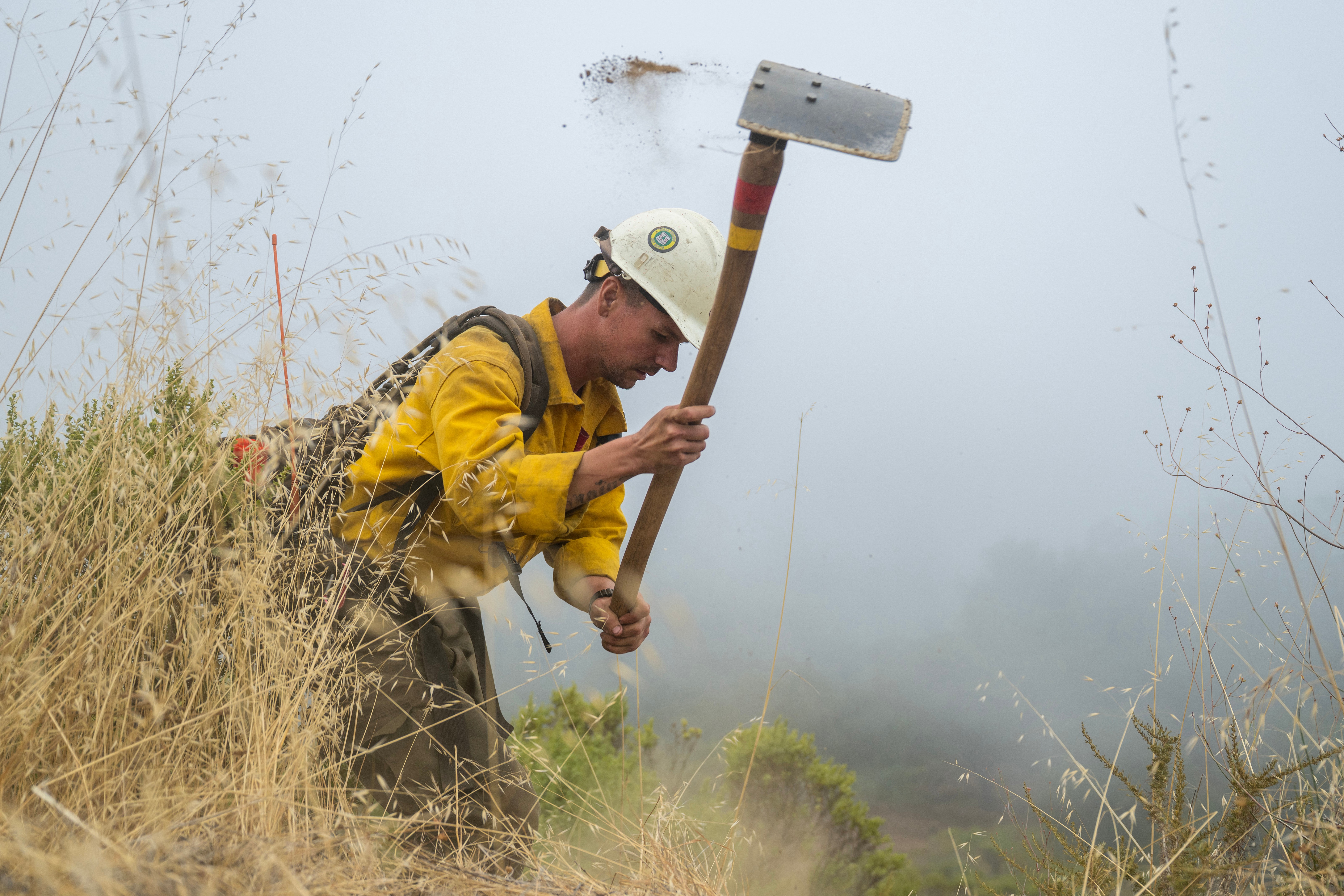 A firefighter cuts a fire break along Coast Ridge Road to help control the Timber Fire in Big Sur, Calif., Thursday, Aug. 13, 2026. (AP Photo/Nic Coury)