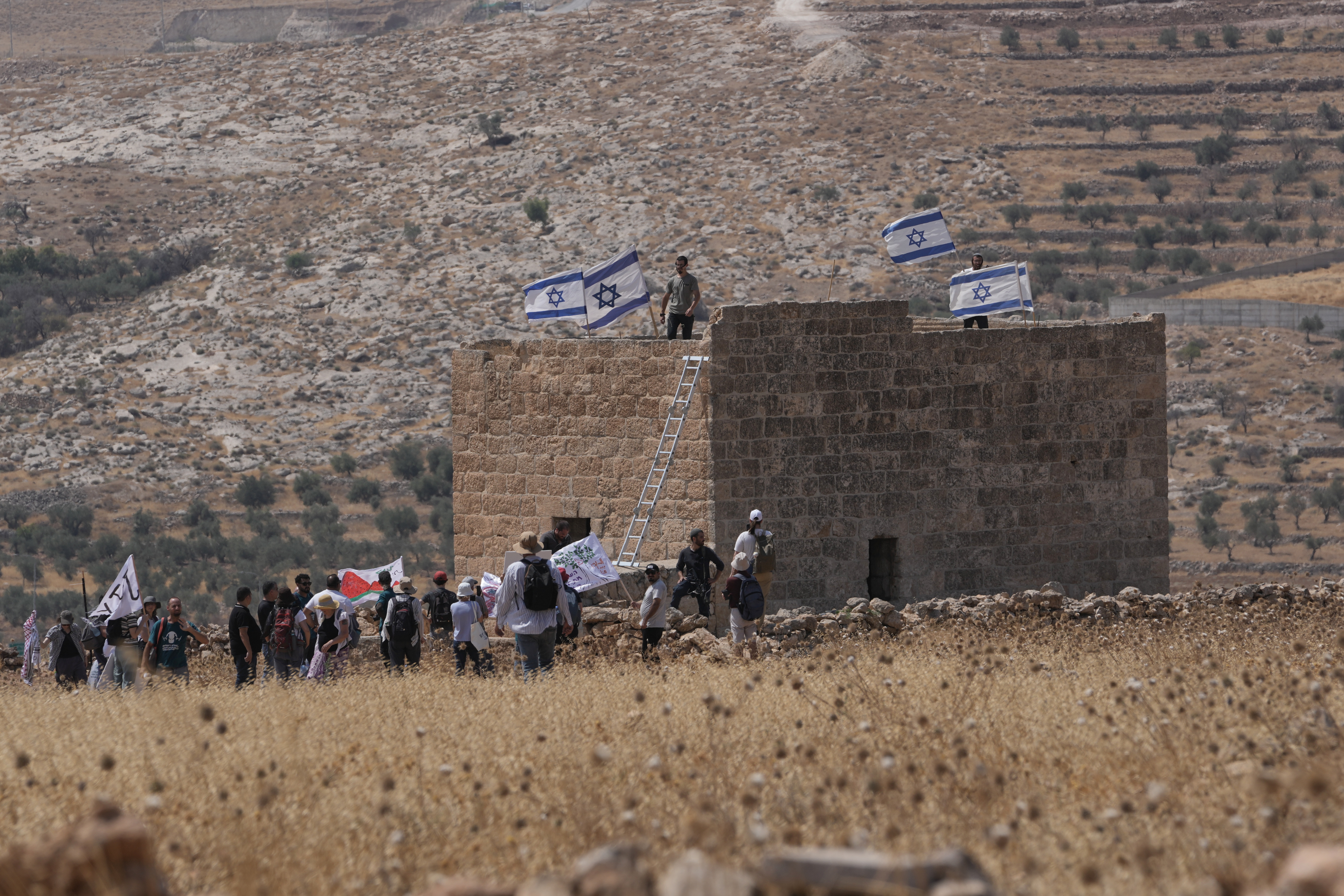 Israeli settlers put up Israeli flags on a Palestinian sturucture after it was taken down by Israeli and foreign peace activists during a protest in support of local landowners whose property is threatened with seizure by settlers, on the outskirts of the West Bank city of Beit Sahour, Friday, Aug. 14, 2026. (AP Photo/Mahmoud Illean)