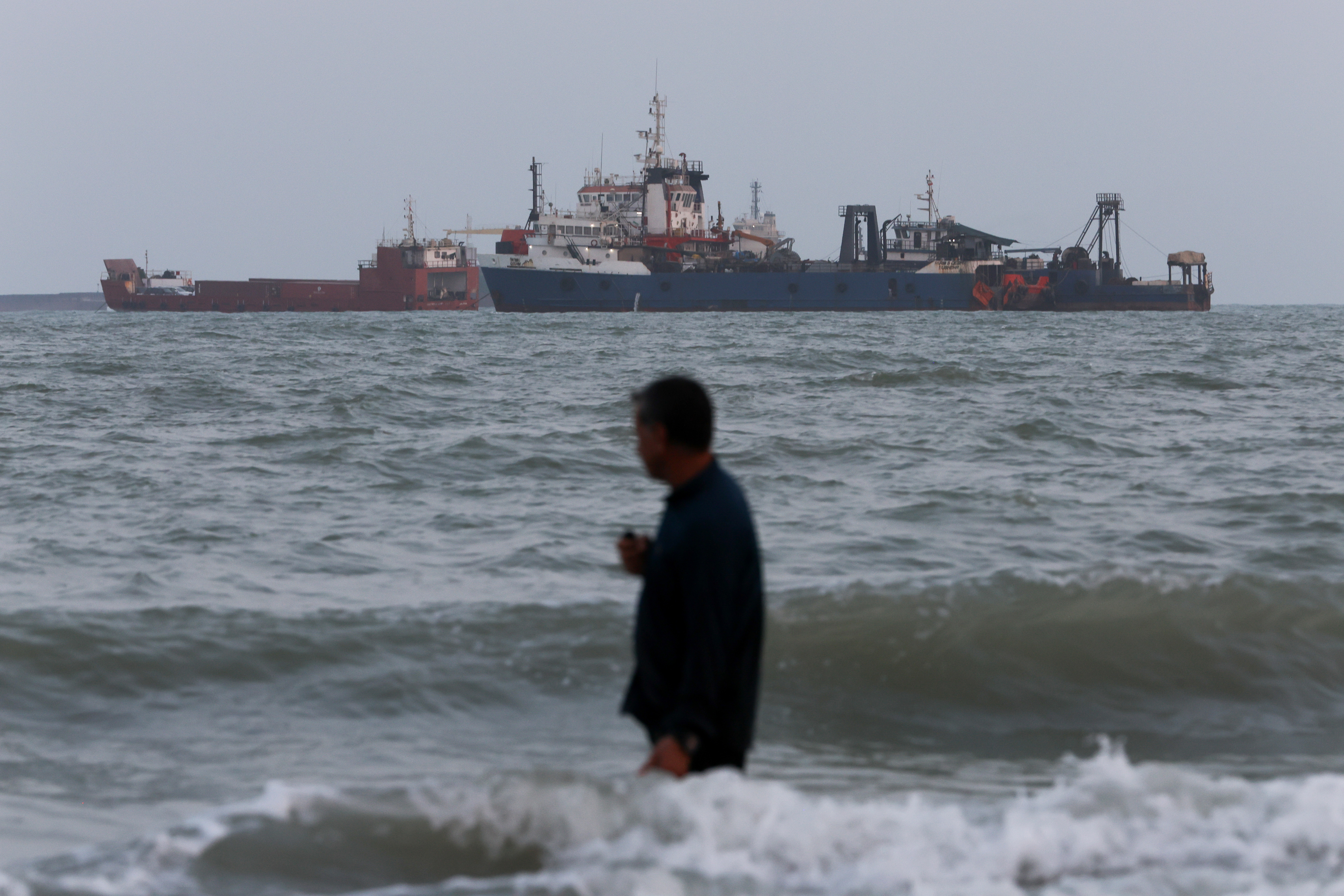 BANDAR ABBAS, IRAN - AUGUST 10: A person wades in the water as ships are seen anchored in the Strait of Hormuz on August 10, 2026 off the coast of Bandar Abbas, Iran. In a recent statement, Iran's Supreme National Security Council said the vital waterway would not reopen until the United States corrects its behavior, demanding that the U.S. end its war on Iran and compensate the country for war damage, among other conditions. Iran has largely halted vessel traffic through the strait with the threat of strikes; meanwhile, the U.S. has imposed a blockade on Iranian ports. (Photo by Ali Saeedi/Getty Images)