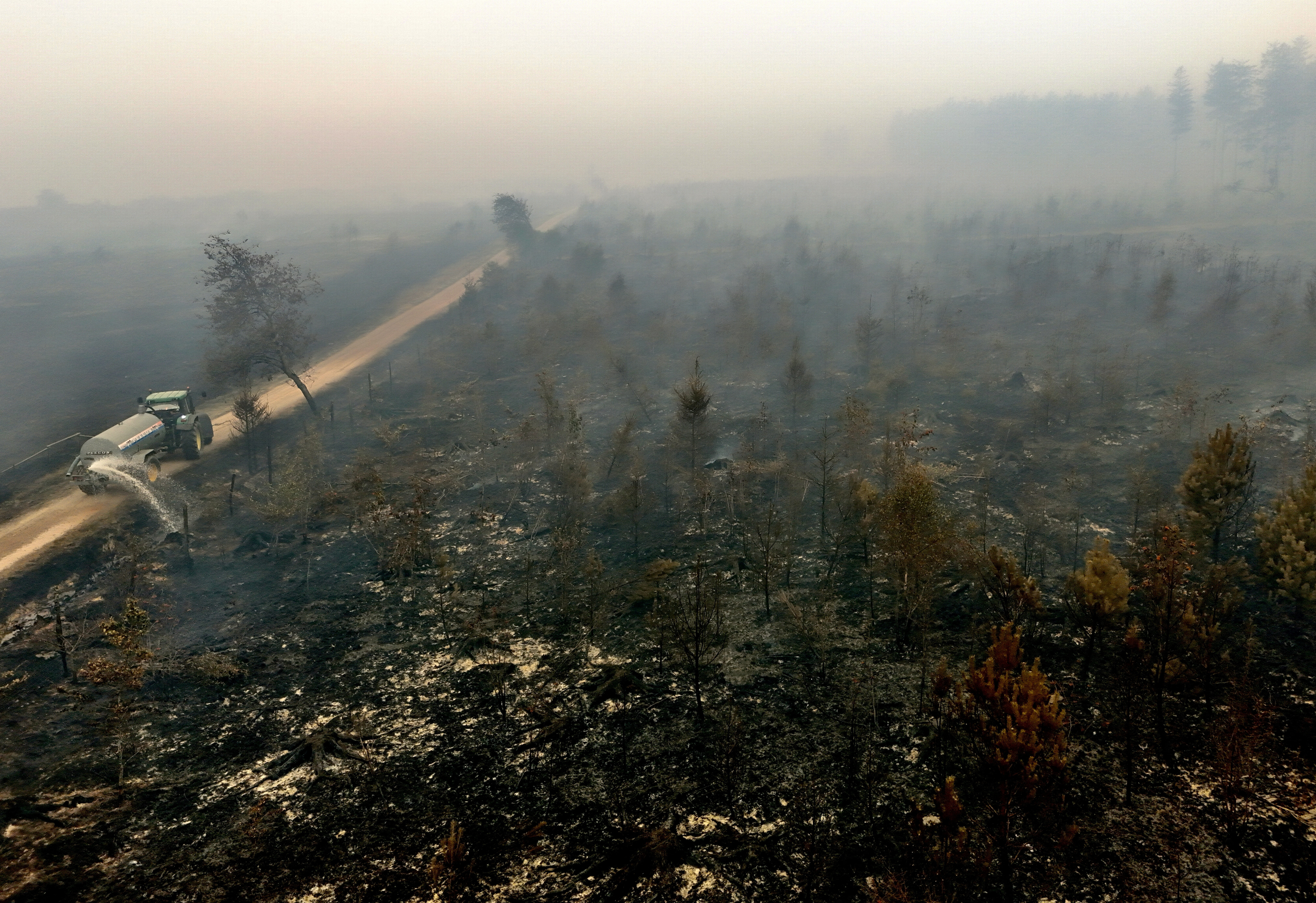 A farmer uses his tractor to spray burned fields and forests during a wildfire near Waimes, Belgium