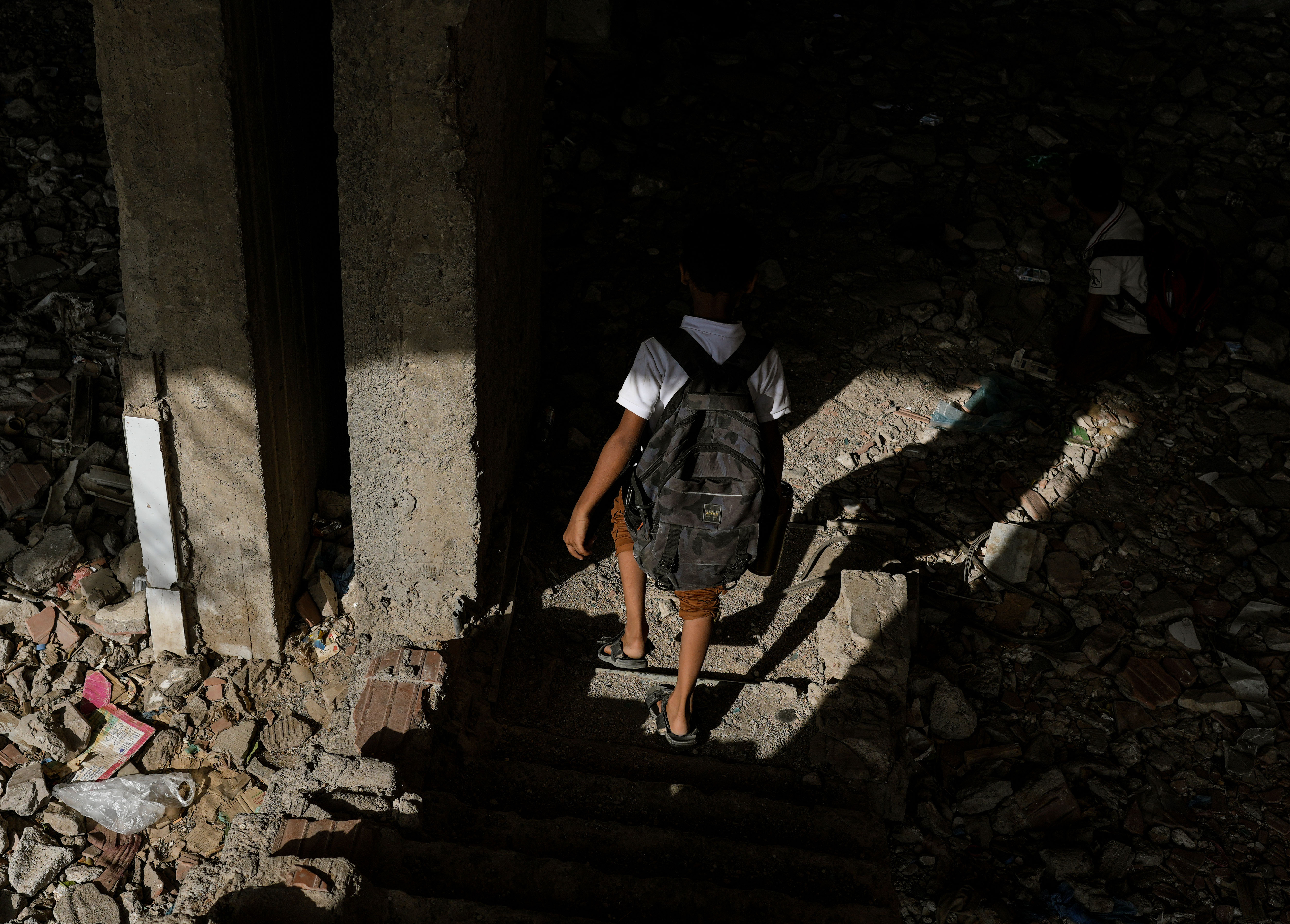 A student carrying a school bag walks through a neighborhood in Aden. Electricity cuts affect education both in overheated classrooms and at home, where studying after dark can depend on rechargeable lamps or small solar systems.