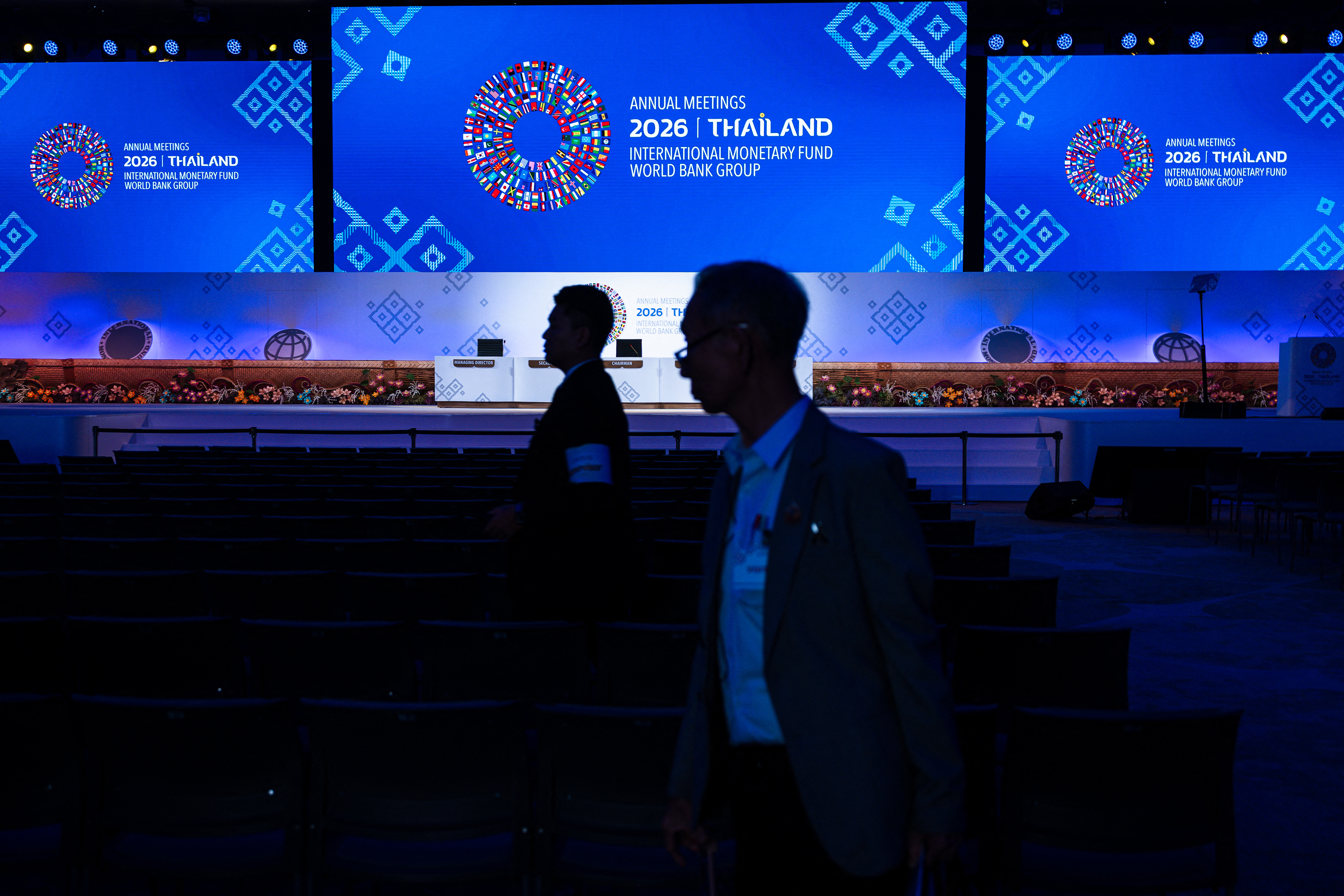 People stand in front of a display featuring the logo of the IMF-World Bank Group Annual Meetings 2026 during preparations for the event at the Queen Sirikit National Convention Center in Bangkok on October 9, 2026. (Photo by Chanakarn LAOSARAKHAM / AFP)