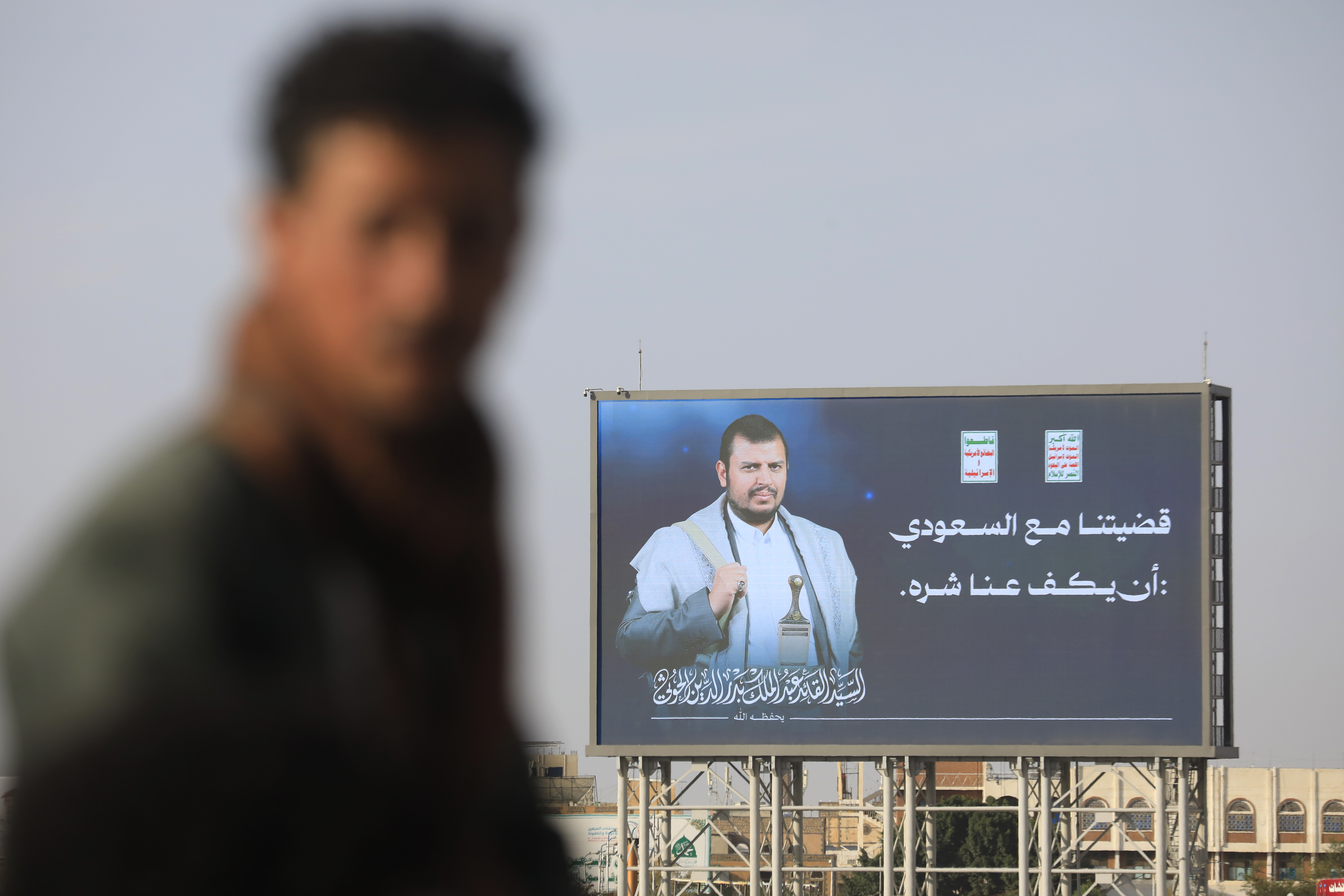 epa13297005 A person walks past a digital billboard featuring Houthi leader Abdul-Malik al-Houthi with a phrase reading in Arabic 'Our dispute with Saudi Arabia is that it stops its harm against us', on a street in Sana'a, Yemen, 11 October 2026. Yemen's Houthis have renewed warnings to airlines against using Saudi airports following a missile attack on Riyadh's King Khalid International Airport on 10 October 2026 that killed 12 people, including four Saudi nationals and eight foreign nationals, and forced the suspension of airport operations, according to Houthi military spokesman Yahya Sarea. EPA/YAHYA ARHAB