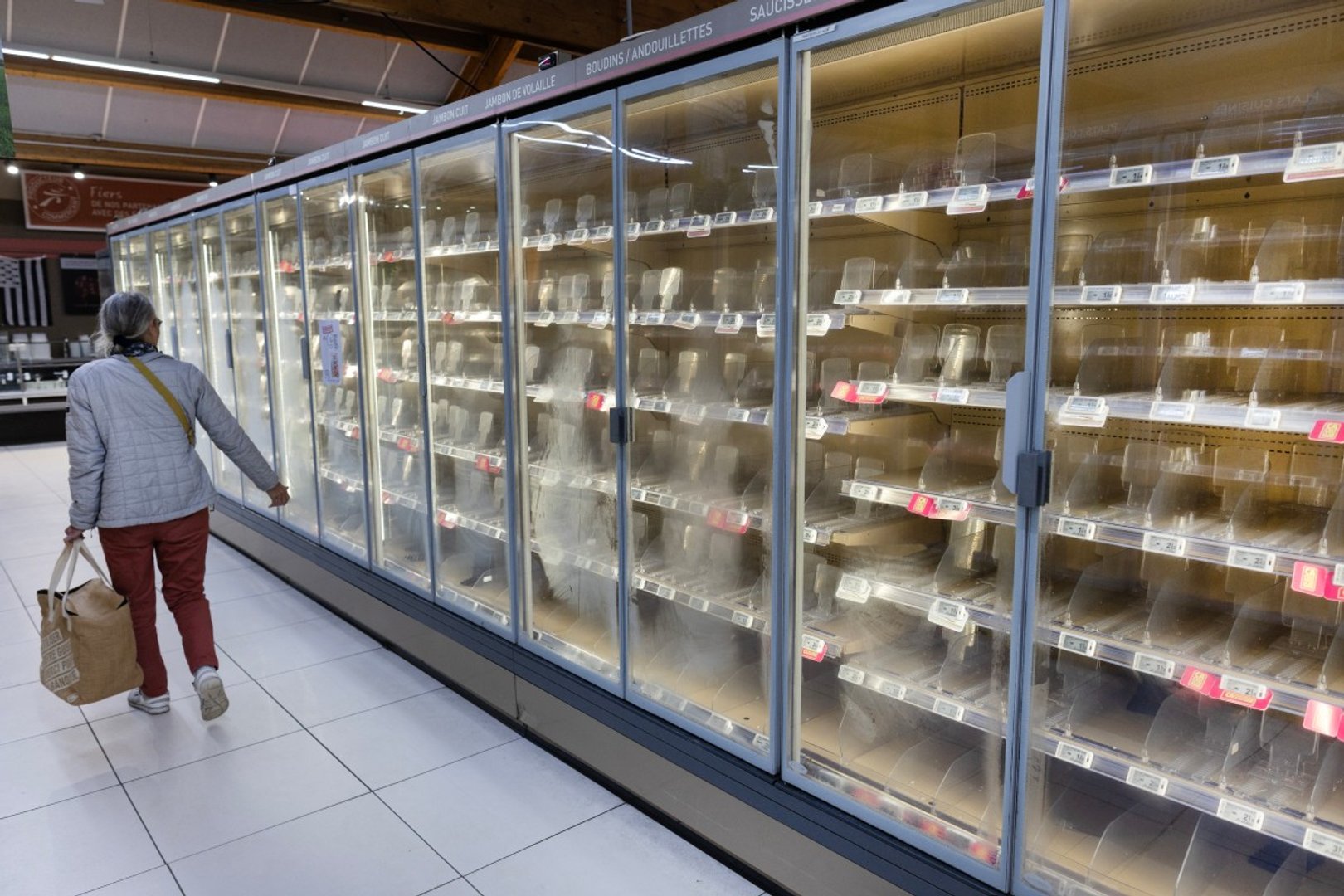 A woman walks past empty fresh-food refrigerators at an Intermarch&eacute; supermarket in N&eacute;vez, western France, on October 12, 2026, following a cyberattack affecting the French supermarket chains Intermarch&eacute; and Cooperative U that caused their refrigerators to defrost. [Photo by FRED TANNEAU / AFP]